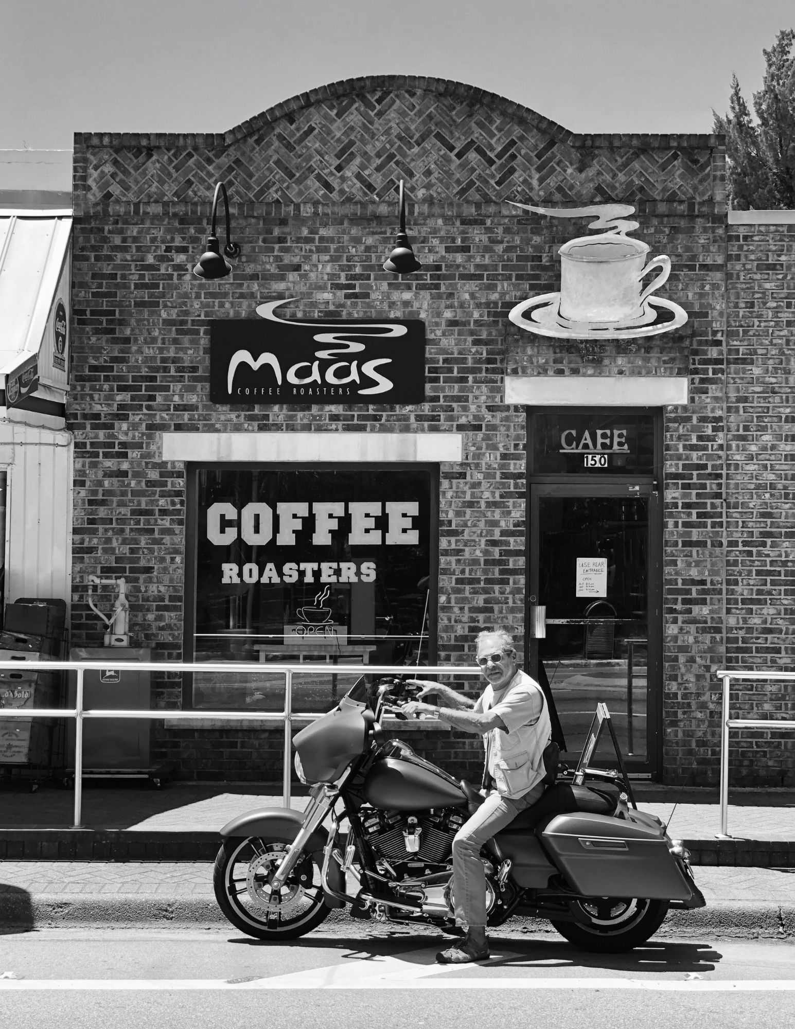 Jim Mass on a motorcycle in front of a coffee shop named 'Maas Coffee Roasters
